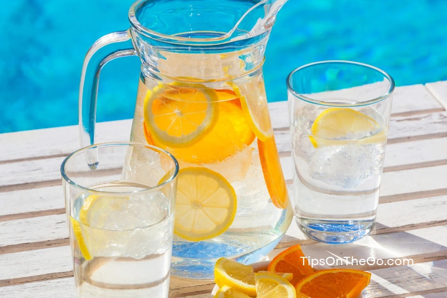 A pitcher of water and two glasses of lemonade next to a swimming pool.