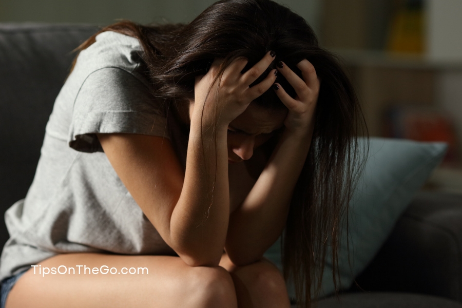 A woman sitting on a couch with her head in her hands feeling depressed.