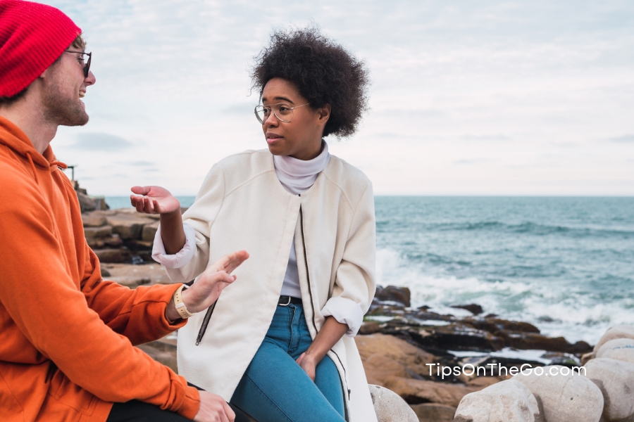 A man and a woman sitting on a stone wall near the ocean having an amazing time. 