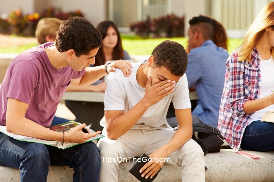 Two friends sitting on a bench while the one tries to comfort the other person.