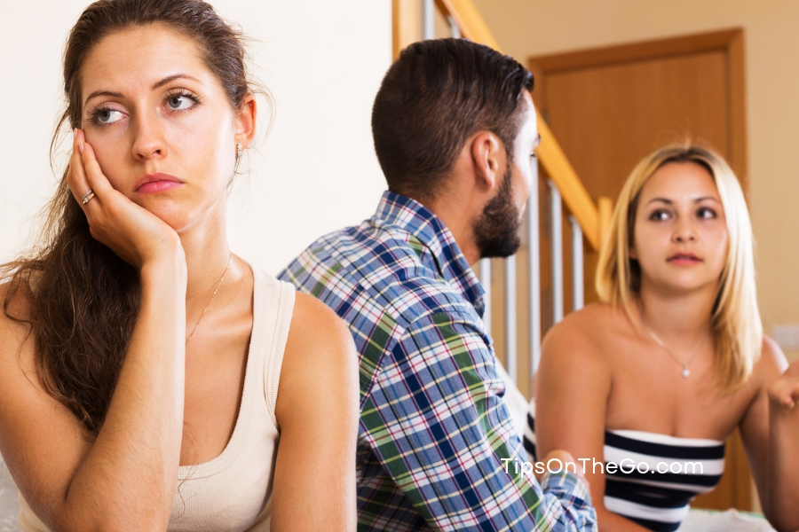 A couple sitting together talking with a woman backing them and having her hand on her face.