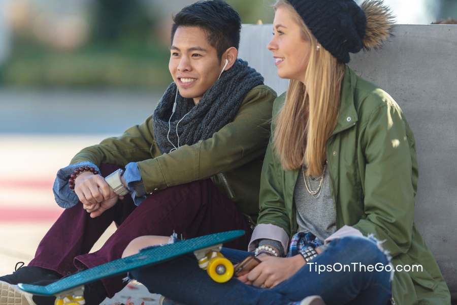 A woman and a man sitting on the ground with skateboard in front of them enjoying each other's company.